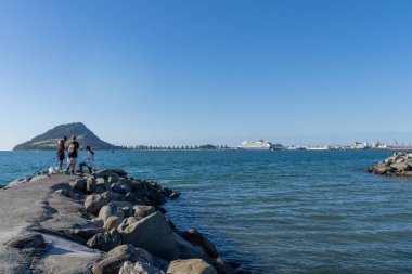 Tauranga Yeni Zelanda - 12 Nisan 2025; Tauranga Limanı ve Maunganui Dağı geçmişi ile dalgakıran sonunda genç balıkçılar.
