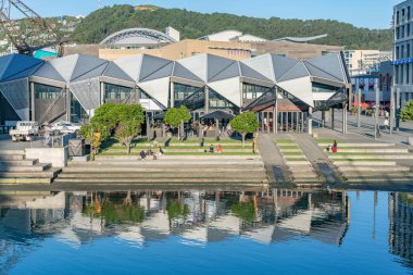 Wellington Yeni Zelanda - 30 Temmuz 2021; Modern bina Whairepo gölüne yansıdı insanların suya ve şehir limanındaki kafelere giden basamaklarda dinlendiği