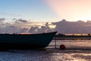 As sunrises and dinghy silhouette over bay at low tide.