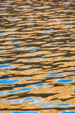Altın ve mavinin desenleri ve şekilleri arka plan veya kavramsal kullanım için gün batımında su yüzeyinde bulanıklaşır