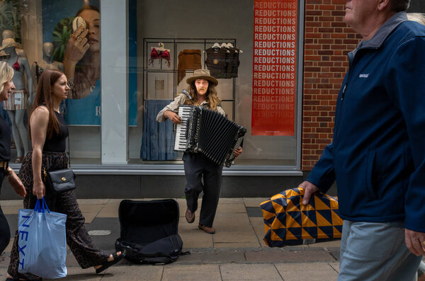 Norwich United Kingdom - 7 июля 2025 года; Уличные сцены Городской пешеходный участок Busker выступает с фортепиано-аккордеоном на пешеходном участке Gentleman 's Walk в городе, когда люди проходят мимо.