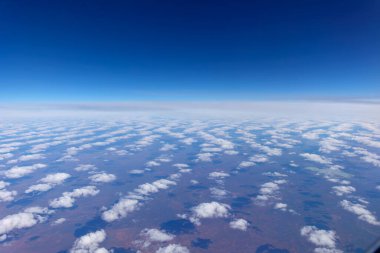 Ufuk çizgisine doğru kaybolan beyaz kabarık bulutlar Avustralya 'nın kırmızı merkezi üzerinde gölgeler oluşturuyordu..