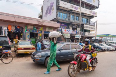 Kigali Rwanda - 4 Eylül 2025; Yeşiller içindeki adam Afrika şehir sahnesinde araba ve motosikletle yolda çuval taşıyor..