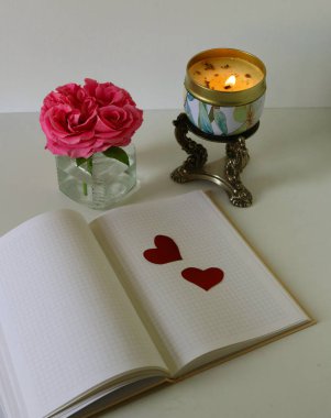 Bir defter, kırmızı bir kalp, bir mum, bir kalem ve bir defter beyaz ahşap bir masada..