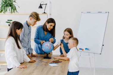 Sınıftaki çocuklar ve öğretmenler küreye bakıyor, öğretmen sınıftaki çocuklara masadaki dersi açıklamaya yardım ediyor. Eğitim okulu süreci, parlak oda ve ilginç öğrenme