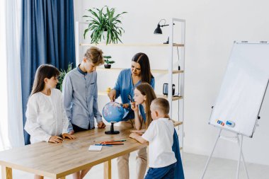 Sınıftaki çocuklar ve öğretmenler küreye bakıyor, öğretmen sınıftaki çocuklara masadaki dersi açıklamaya yardım ediyor. Eğitim okulu süreci, parlak oda ve ilginç öğrenme