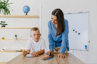 Private lesson. Attentive young woman tutor teacher helping little boy pupil with studying, correct mistakes explain learning material. Smiling mother assist small boy with home task