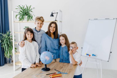 Sınıftaki çocuklar ve öğretmenler küreye bakıyor, öğretmen sınıftaki çocuklara masadaki dersi açıklamaya yardım ediyor. Eğitim okulu süreci, parlak oda ve ilginç öğrenme