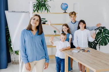 Birlikte gülümsüyoruz. Farklı yaşlarda bir grup çocuk okulda öğretmenle birlikte geniş bir sınıfta duruyor..