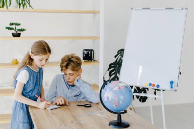 Genç bir kız ve oğlan, sınıflarında dünya ile birlikte masanın yanında oturuyorlar. Okul çocuğu ve liseli kız okulda birlikte proje yapıyorlar.