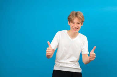 Mükemmel bir iş. Kameraya gülümseyen, el işaretini onaylayan ve sonuçtan memnun olan memnun bir adam. Mavi arka planda kapalı stüdyo çekimi