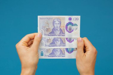 Image woman's hands which holds British pounds in her hands isolated over blue studio background