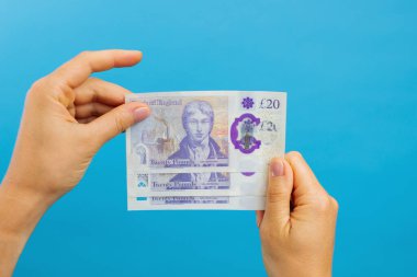Image woman's hands which holds British pounds in her hands isolated over blue studio background