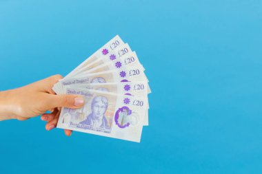 Image woman's hands which holds British pounds in her hands isolated over blue studio background