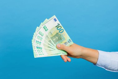Woman's hand holding hundred euros banknotes isolated on blue background. Euro money, cash banknotes