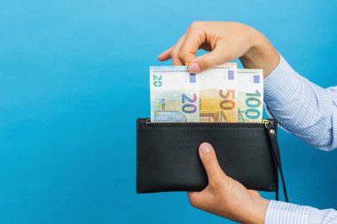 Female hands holding black wallet with euro banknotes on a blue background