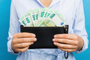 Female hands holding black wallet with euro banknotes on a blue background