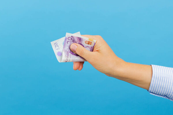 Woman's hand holding twenty british pounds banknote isolated on blue background. British pounds money, cash banknote