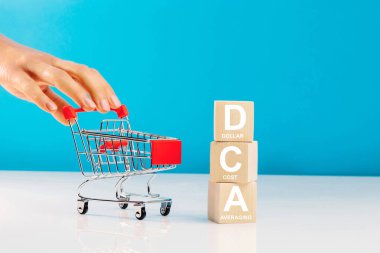 DCA, ahşap küplere ve stüdyodaki boş alışveriş arabalarını mavi arka planda iten kadınlara yazılmıştır. İş konsepti. DCA - ortalama maliyet ortalamasının kısaltması