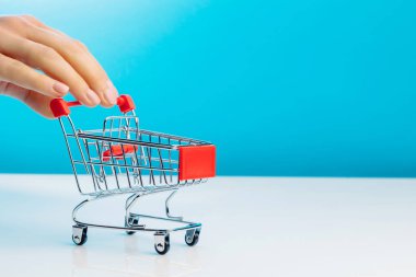 İş ve e-ticaret kavramı. Stüdyoda mavi bir arka planda dururken boş bir alışveriş arabasını iten parmakları kullanarak yakın plan. Yan görüş. Metin için boşluk