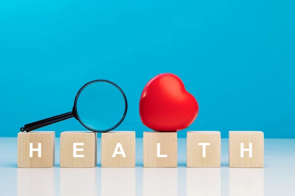 stock image Red heart and magnifying glass on top of wooden cubes with the word HEALTH on a table in studio