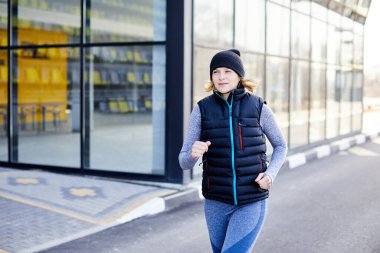 Genç ince bir kız baharın başlarında parkta koşar. Spor kulübünün yakınında koşan çekici bir kadın.