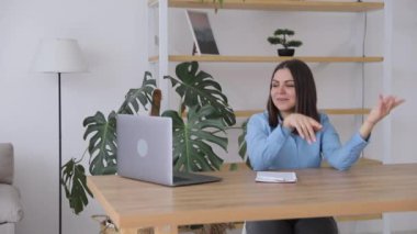 Young smiling woman in casual clothing dancing in living room near table with laptop
