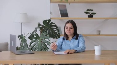 Young female dreamy thoughtful student looking away working on laptop in office coworking space classroom. Student using computer for remote learning online training.