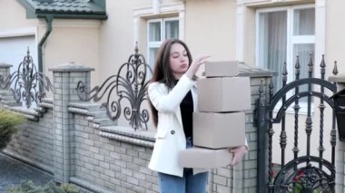 Young woman carrying parcels home, standing with a heap of cardboard boxes. Concept of buying goods online and delivering them home