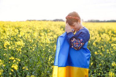 Ukrayna için dua et. Kolza tarlasında Ukrayna bayrağı taşıyan bir çocuk. Ulusal bayrak tutan kız barış için dua ediyor.