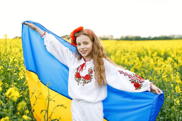 Pray for Ukraine. Child with Ukrainian flag in rapeseed field. Girl holding national flag praying for peace.