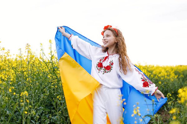 Pray for Ukraine. Child with Ukrainian flag in rapeseed field. Girl holding national flag praying for peace.