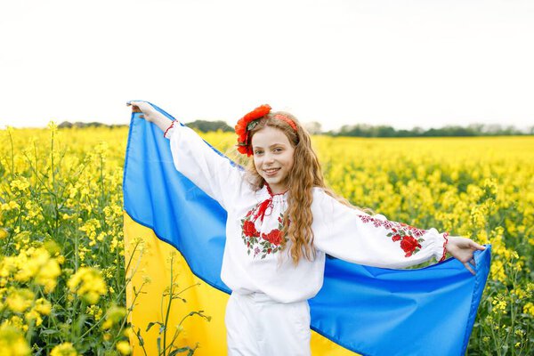 Pray for Ukraine. Child with Ukrainian flag in rapeseed field. Girl holding national flag praying for peace.
