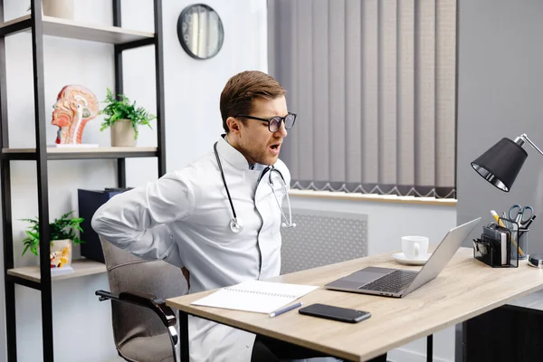 Young Male Doctor Sits His Workplace Feels Pain His Back — Foto Stock