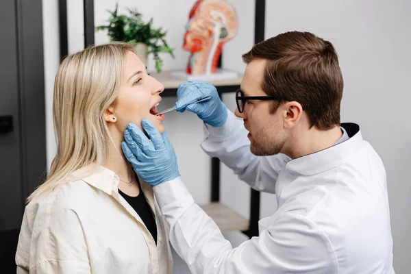 Doctor using inspection spatula to examine patient throat. ENT doctor doing throat exam of a woman. Patient opened her mouth to throat check-up.