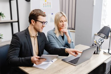 Modern ofis içinde buluşmaya başla, laptop ve tablet üzerinde çalış. Genç bir kadın ve bir adam masada oturuyor ve bir iş projesi üzerinde çalışıyorlar..