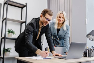 Concentrated male businessman looking at computer monitor, working with a young female worker on a project, people holding a video meeting with a client or interviewing a job candidate