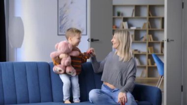 Mutlu hamile kadın kanepeye oturmuş gülümsüyor ve hafta sonu evde zıplayan çocukla oynuyor.