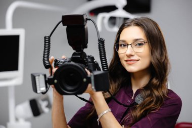 Kadın dişçinin portresi, elinde fotoğraf makinesi, dişçi ofisinde duruyor..