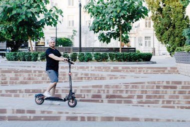 Beyaz beysbol şapkalı genç yakışıklı adam, şehirde işe giderken scooter 'a biniyor. Aktif yaşam tarzı, sırt çantalı gezgin. Ekoloji ve temiz ekolojik ulaşım biçimi