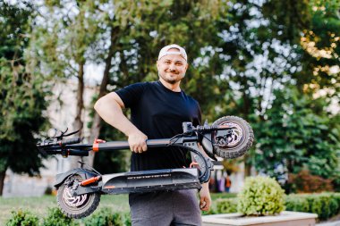 Adam katlanır pozisyonda elektrikli scooter taşıyor. Merdivenlerde elinde katlanır bir E-Scooter taşıyan adam. Erkek şık kıyafetler giyer ve elektrikli scooter kullanır..