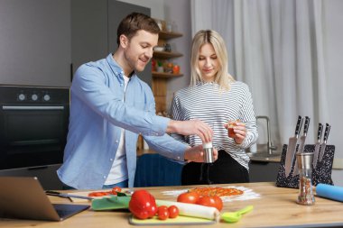 Romantik çift mutfakta yemek pişiriyor. Yakışıklı adam ve çekici genç kadın salata ve pizza yaparken birlikte eğleniyorlar. Sağlıklı yaşam tarzı kavramı