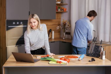 Kocası bulaşıkları yıkarken güzel bir kadın mutfakta salata pişiriyor.