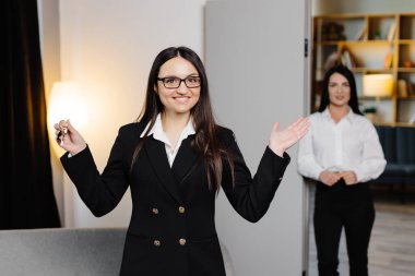 Emlakçı, elinde anahtarları olan bir emlakçı. Bir emlak dairesinin arka planında.