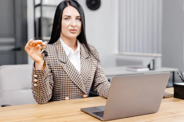 Young happy employee business woman wearing suit sitting at office desk with laptop and giving key in office.