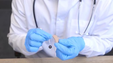 Bir otolaringolog elinde işitme cihazı tutuyor. Doktor hastaya danışıyor.