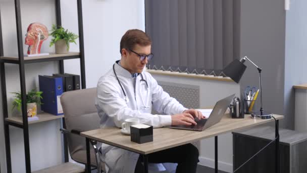 医生坐在他工作的地方的办公桌前 用笔记本电脑工作 完美的医疗服务在诊所 医疗和医疗保健的美好未来 — 图库视频影像