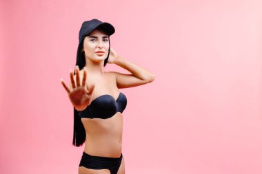 Slim woman in black swimsuit and cap showing a stop gesture with his hand and posing isolated on pink background. People summer vacation rest lifestyle concept.