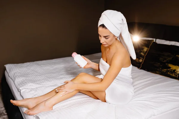 在家里的卧室里 一位漂亮的白人年轻女子在床上用自己的腿涂了些护肤霜 美容美发的女人洗完澡也有护肤功能 — 图库照片