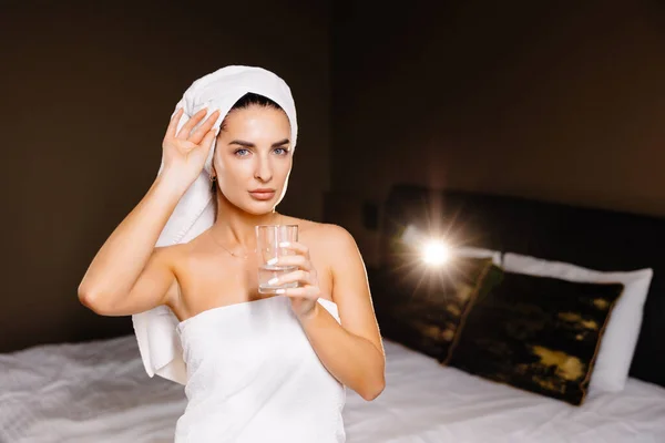 在家里洗澡后 年轻的安详的女人带着浴巾喝水 美容治疗 水合作用概念 — 图库照片